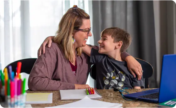 Mother and son smiling at each other while working with their laptop at home