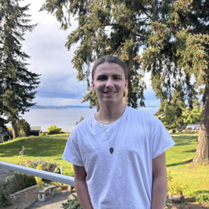 A photo of Foster Peterson, a white male wearing a white t-shirt, standing outside. 