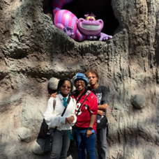 Jahzara and two family members pose in front of a wall with a plastic cheshire cat grinning above them.