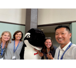 Four coworkers are posing for a photo with a person in a whale mascot suit.
