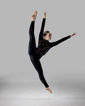 A teenage girl in a black leotard is shown in the air executing a dance move.