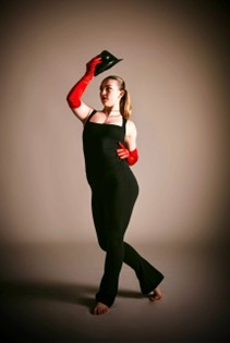 A teenage girl wearing a black outfit with bright red gloves is posing while holding a top hat above her head.